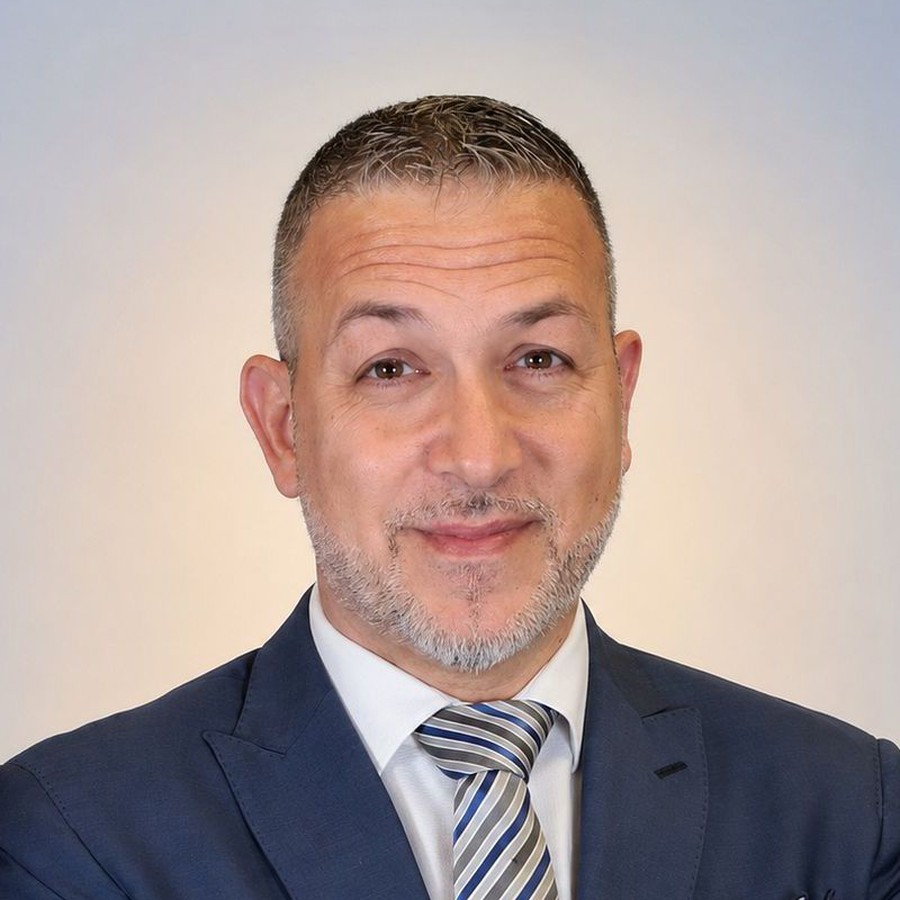 Ritratto di Marco Iacovitti in giacca blu, camicia bianca e cravatta a righe, barba brizzolata su sfondo chiaro